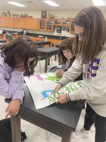 Freshman STUCO members Sophie DeClue, Macy Saunders, and Maya Porter finish the Thursday homecoming theme poster, Monsters University:  The Trojans are Going to School the Blackcats.